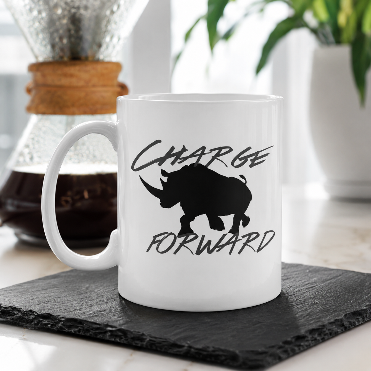 A white ceramic coffee mug with a black rhinoceros silhouette and the words 'CHARGE FORWARD' printed on the side, sitting on a dark slate coaster in a kitchen setting.