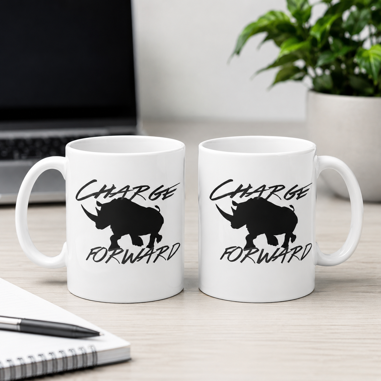 Two white ceramic mugs with black rhinoceros silhouettes and the words 'CHARGE FORWARD' printed on them, displayed side by side on a light wood desk with a laptop, notebook, and plant in the background.