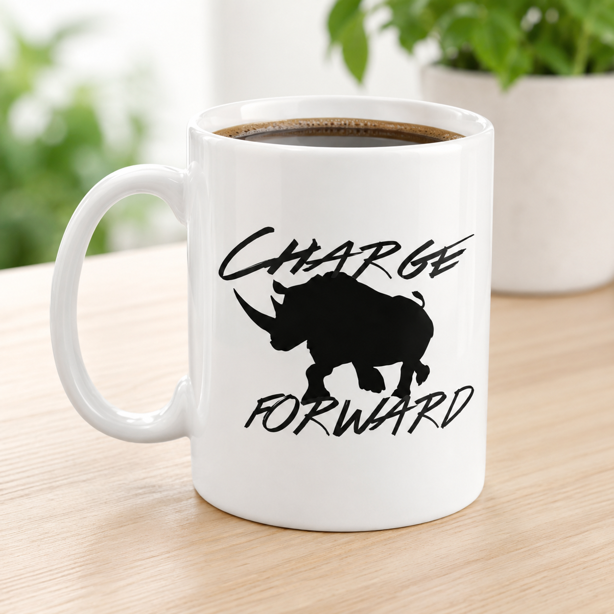A white ceramic coffee mug with a black rhinoceros silhouette and the words 'CHARGE FORWARD' printed on the side, filled with black coffee and sitting on a light wood table with a blurred plant in the background.