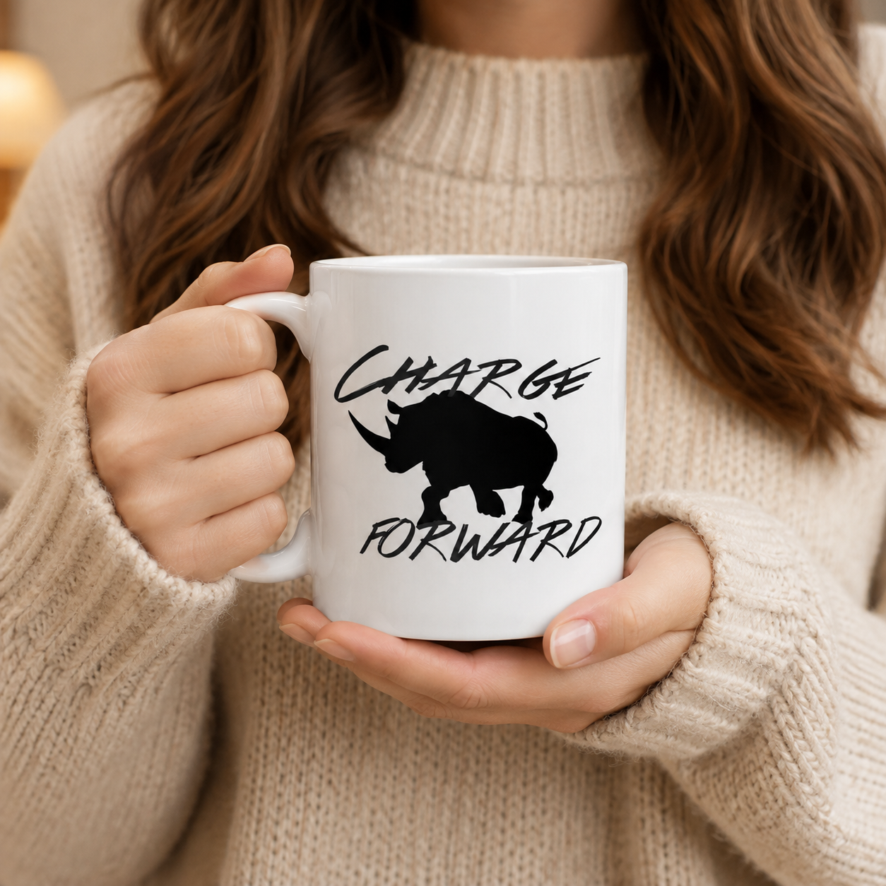 A person in a beige knit sweater holds a white ceramic mug with a black rhinoceros silhouette and the words “CHARGE FORWARD” printed on the front.
