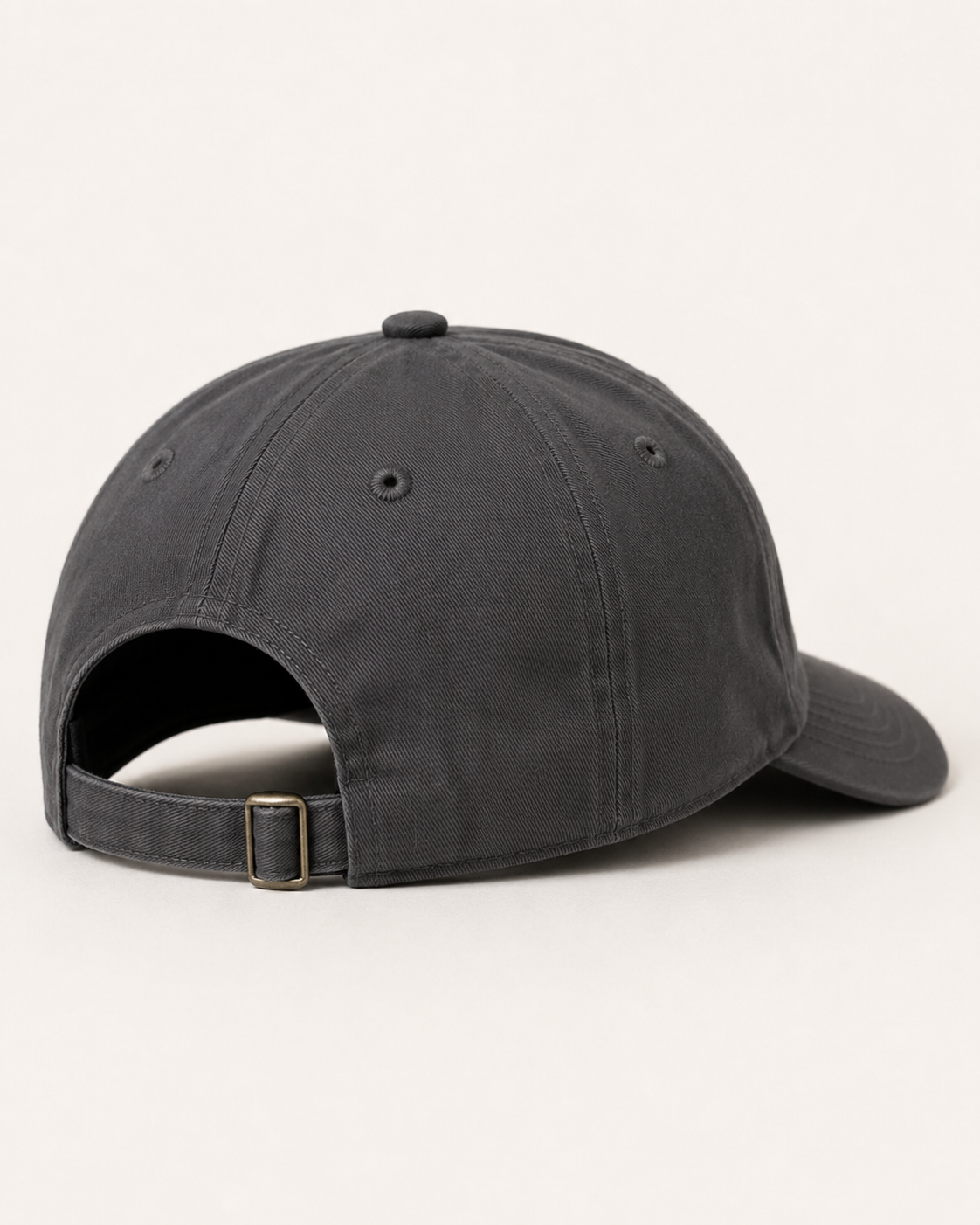 A dark charcoal gray cotton baseball cap shown from a three-quarters back angle, featuring an adjustable strap with a small gold-tone metal buckle on a clean off-white background.