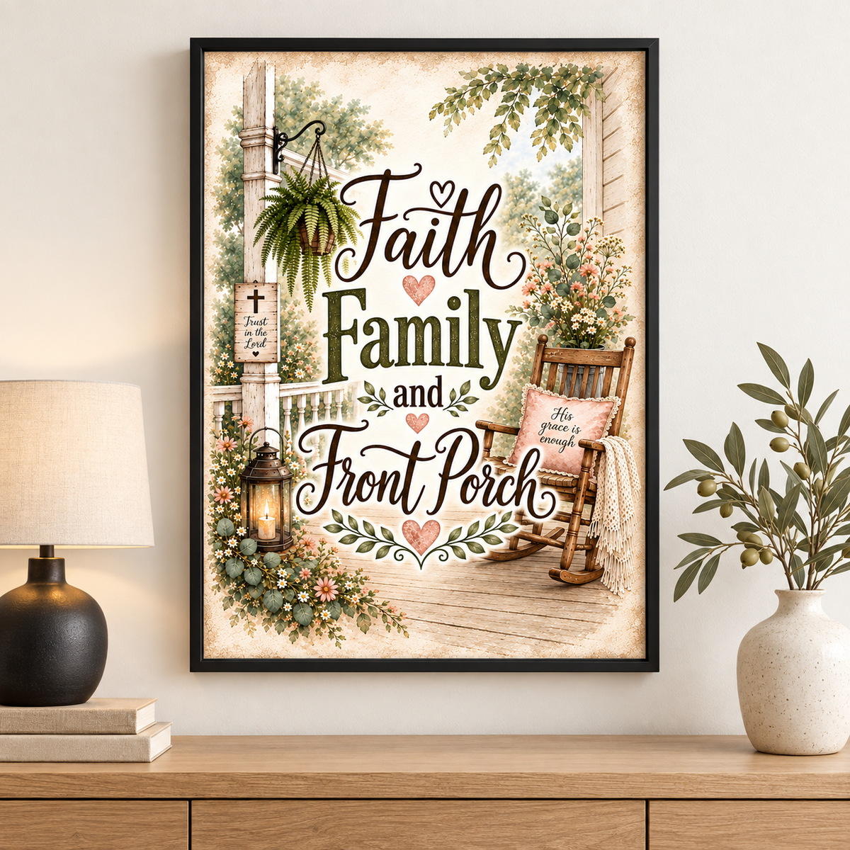A framed art print featuring the text 'Faith Family and Front Porch' in decorative script over a vintage porch scene with a rocking chair, lantern, flowers, and greenery. The framed print is displayed on a wooden console table in a styled room setting with a lamp on the left and a vase with branches on the right.