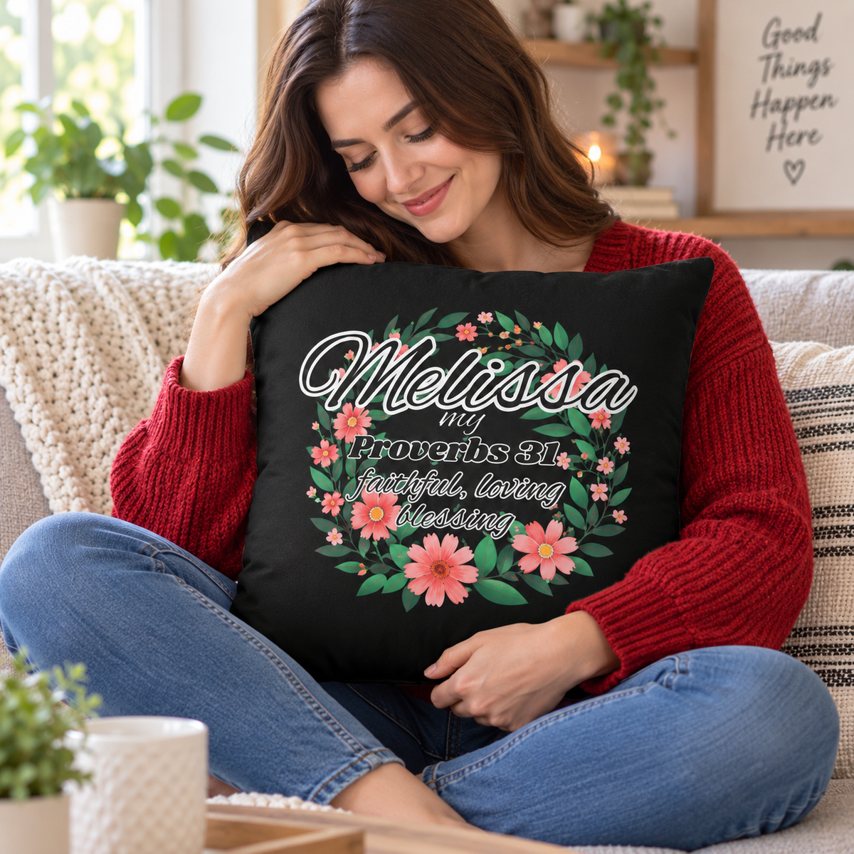 A woman sitting on a couch holding a black decorative throw pillow with a floral wreath design and the text 'Melissa my Proverbs 31:10 faithful, loving blessing'.