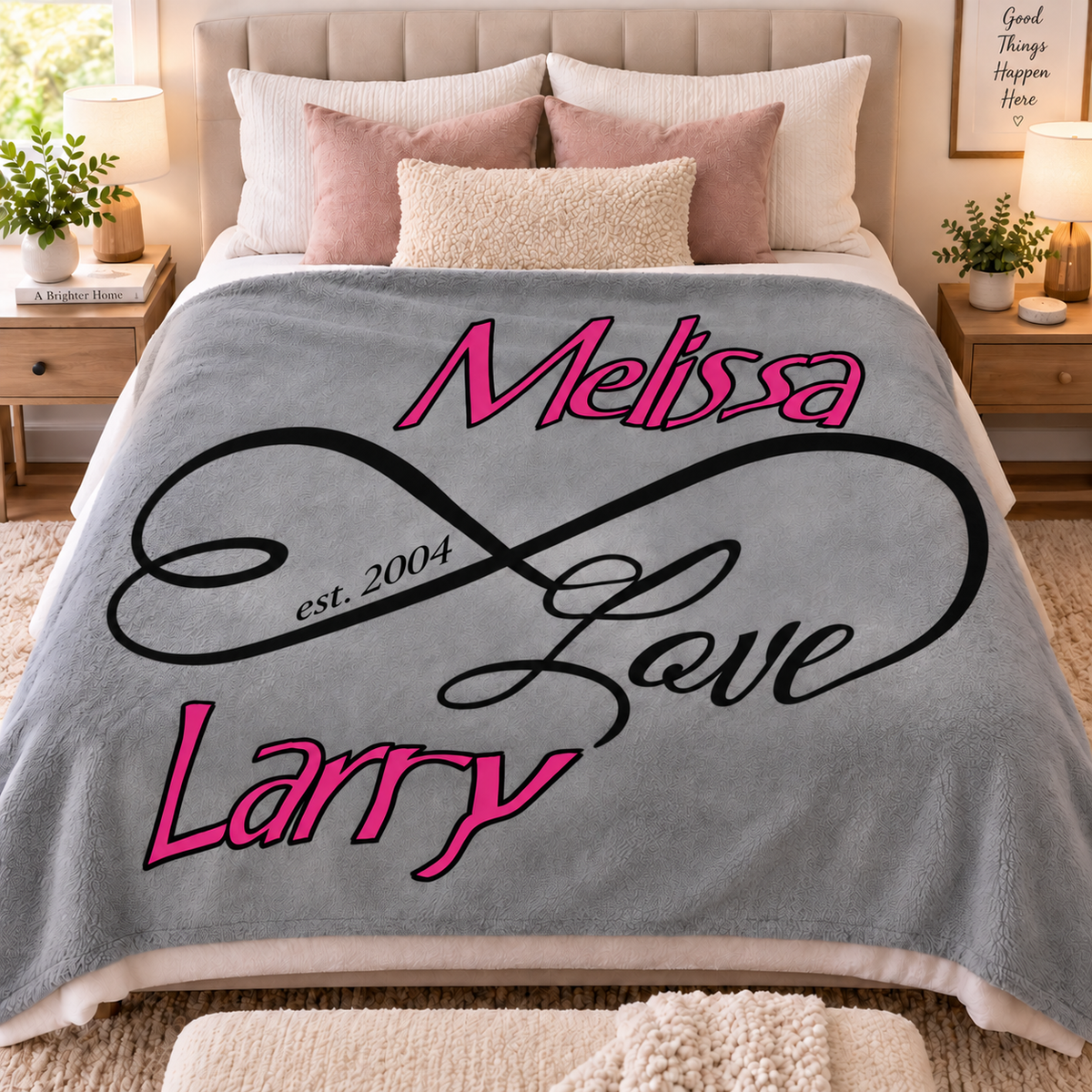 A personalized gray fleece blanket draped over a bed in a styled bedroom. The blanket features the names 'Melissa' and 'Larry' in bright pink script, with 'Love' in black cursive and 'est.
