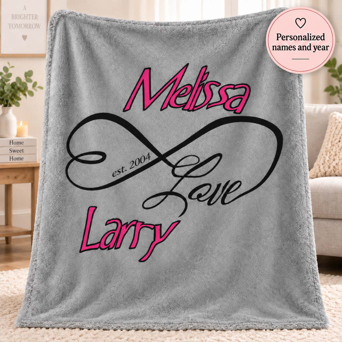 A gray fleece throw blanket draped over a chair in a living room setting, featuring a personalized design with the names 'Melissa' and 'Larry' in pink script, a black infinity loop with 'Love' in black script, and 'est. 2004' printed inside the loop.