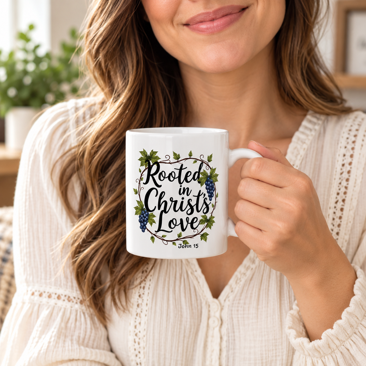 A woman in a cream knit sweater holds a white ceramic mug with a printed design that reads 'Rooted in Christ's Love' with grapevine leaves and blue grapes, and 'John 1:13' below.
