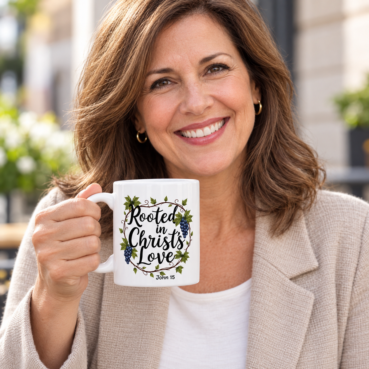 A smiling woman holding a white ceramic mug with a floral design and the text 'Rooted in Christ's Love John 15' in an outdoor setting.