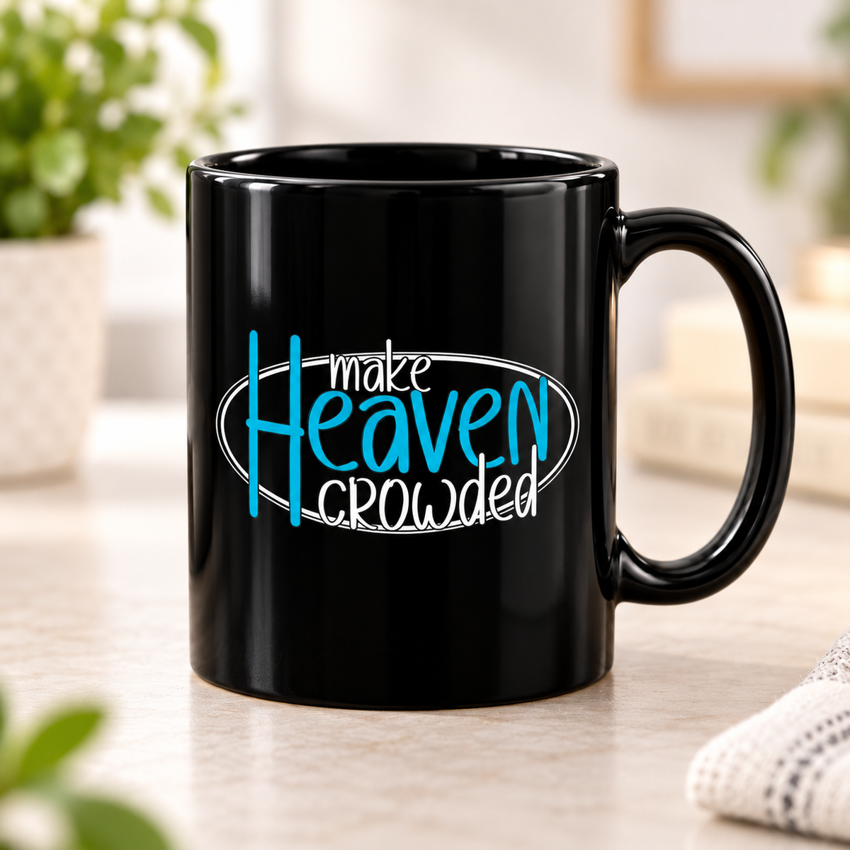 A glossy black ceramic mug with the phrase 'make Heaven crowded' printed on the side in white and bright blue lettering, set on a light tabletop with a softly blurred indoor background.