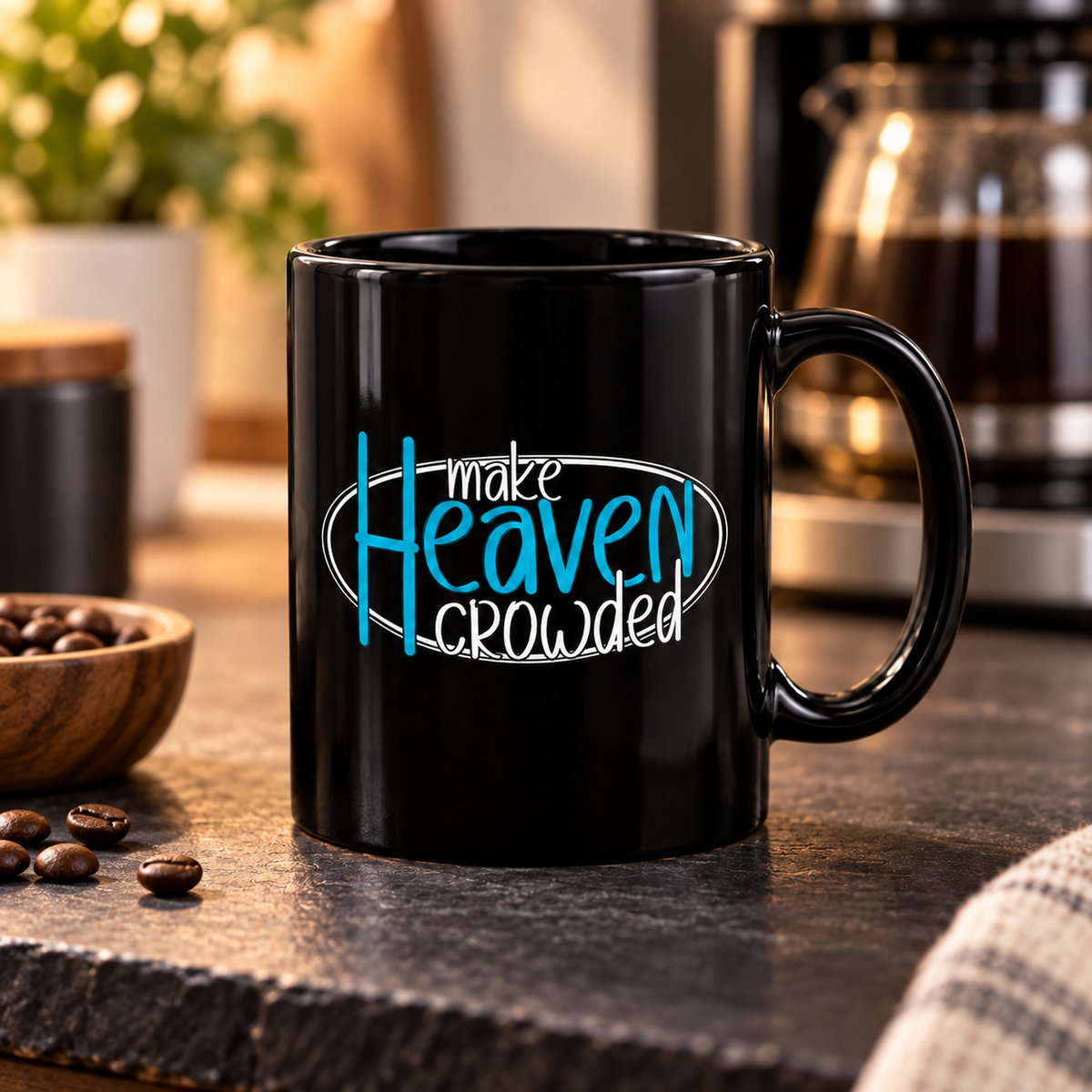 A black ceramic coffee mug with the text 'make Heaven crowded' printed on the side, styled on a dark stone surface with coffee beans and a coffee maker in the background.