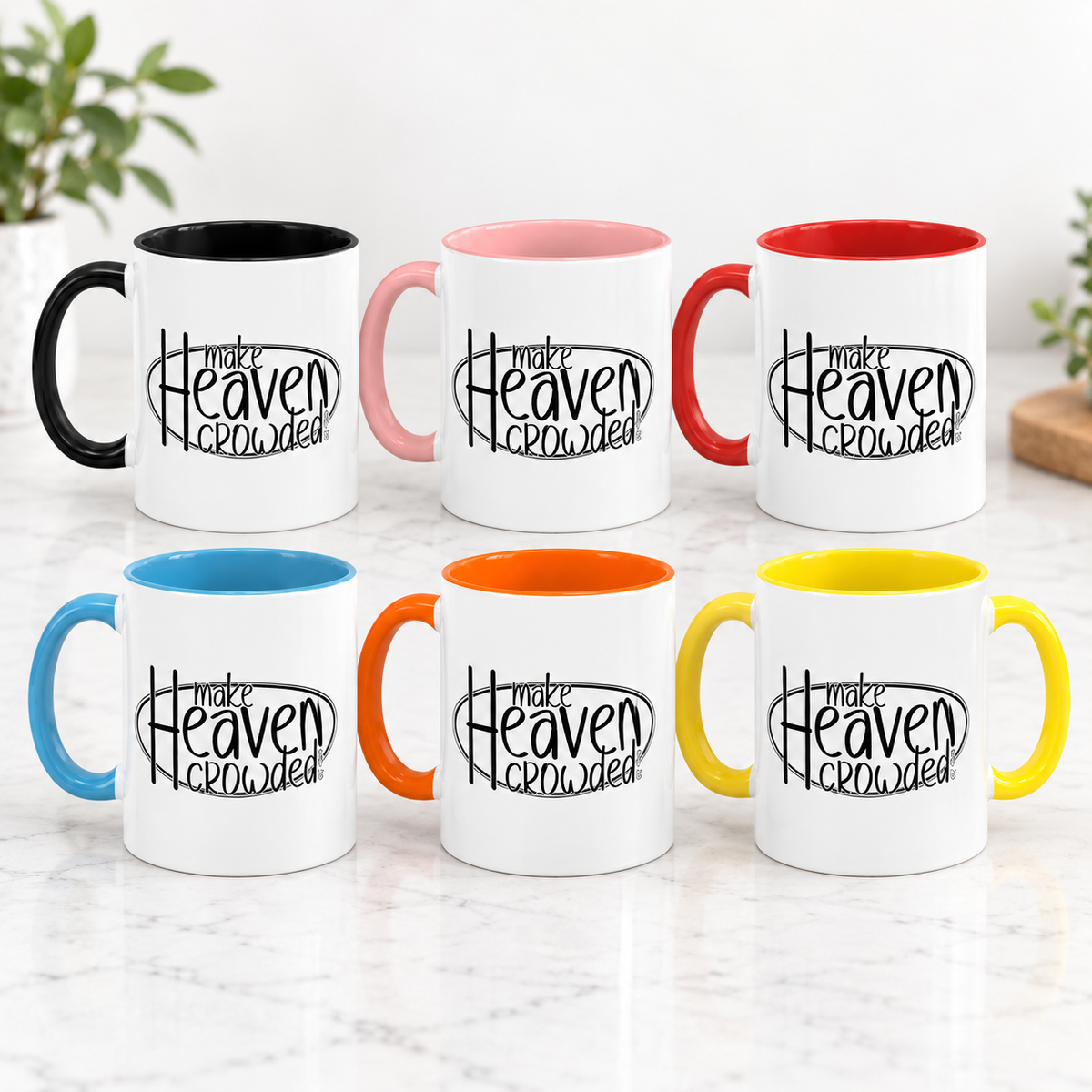 Six ceramic mugs arranged in two rows on a light marble surface, each with a white exterior, black printed text reading 'make Heaven crowded,' and a different handle/interior color: black, pink, red, blue, orange, and yellow.
