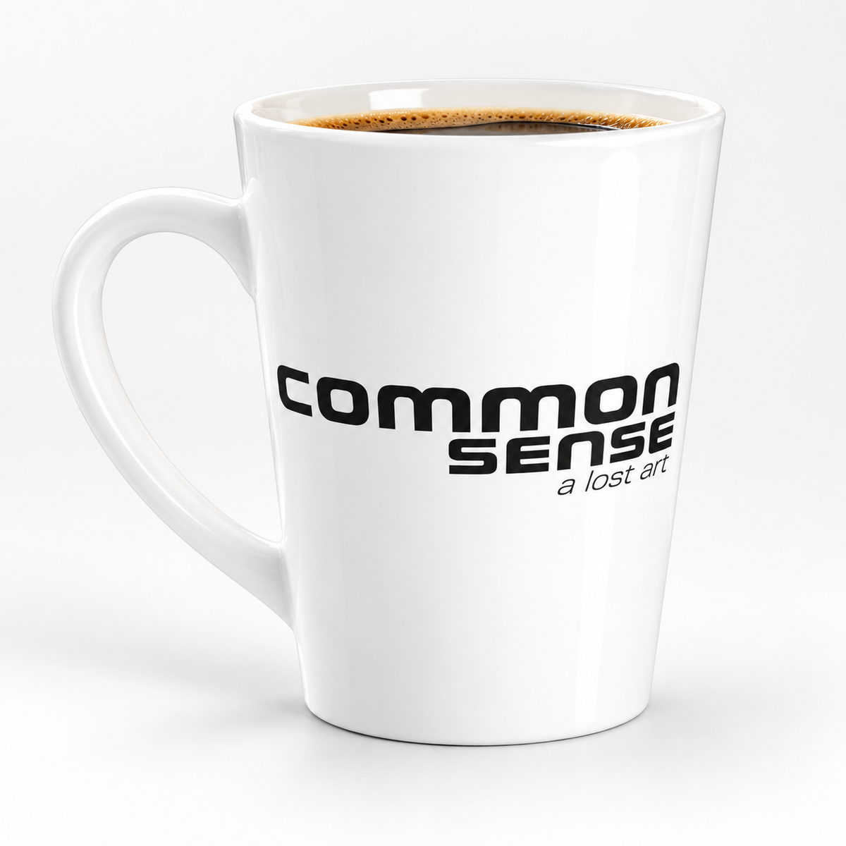 A white ceramic latte mug filled with coffee, featuring the black printed text 'COMMON SENSE' and 'a lost art' on the front, set against a clean white background.