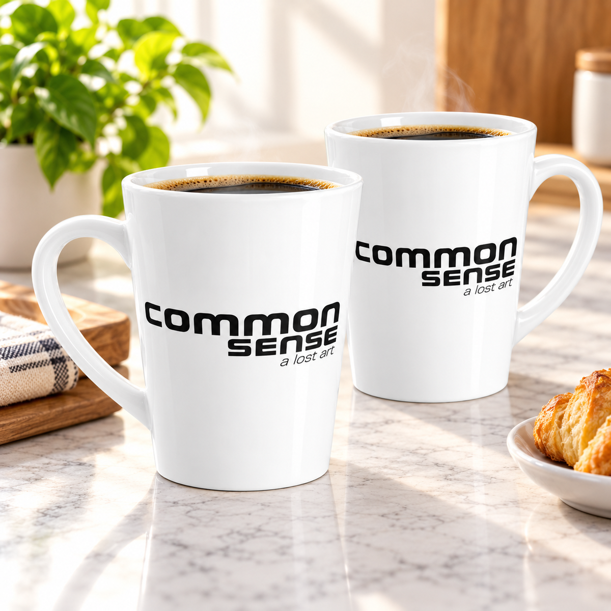Two white ceramic coffee mugs filled with black coffee sit on a marble countertop in a kitchen setting. The mugs are printed with the phrase 'common sense a lost art' in black text.
