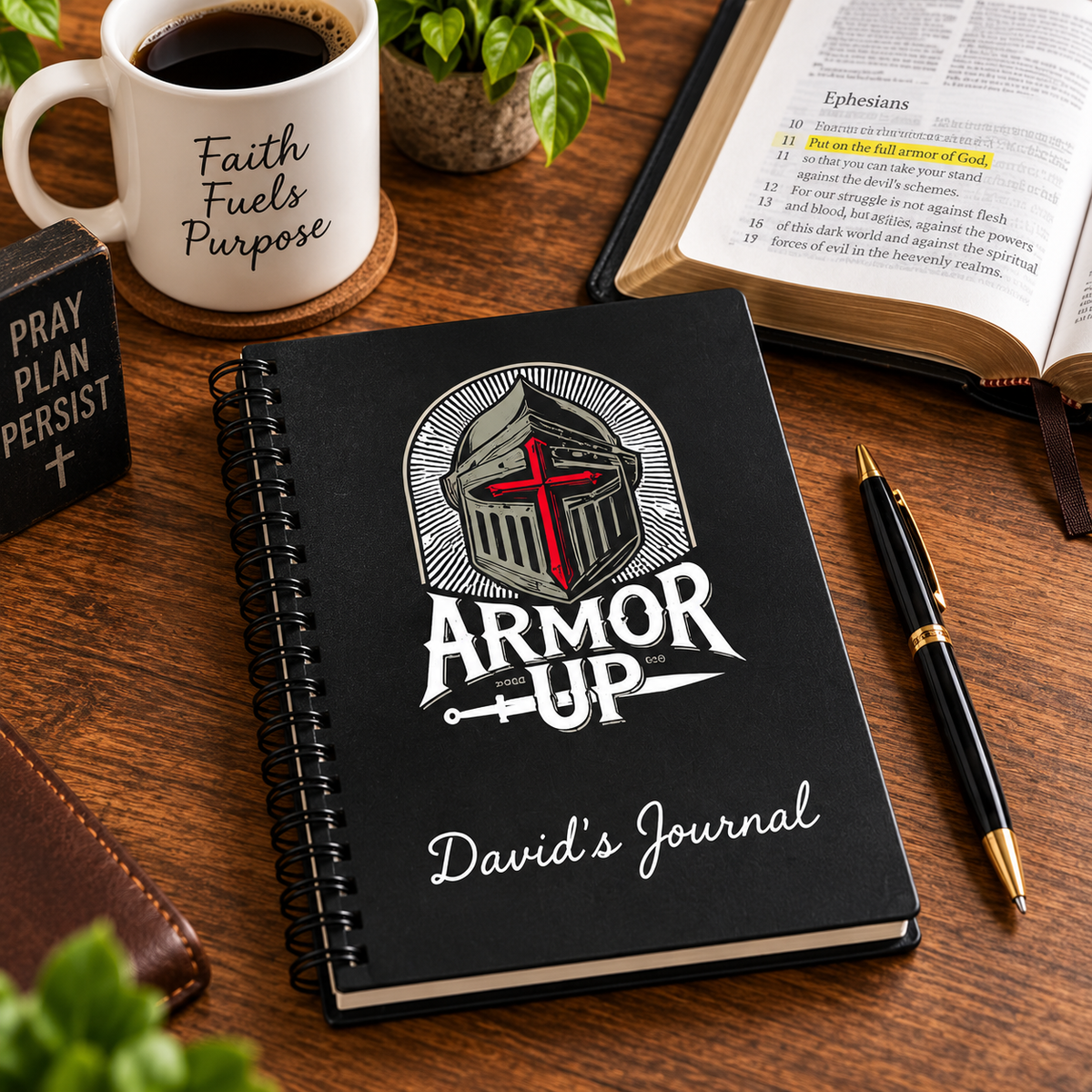 A black spiral-bound journal titled 'David's Journal' with a knight helmet and red cross graphic, displayed on a wooden desk with a coffee mug, Bible, pen, and other desk accessories.