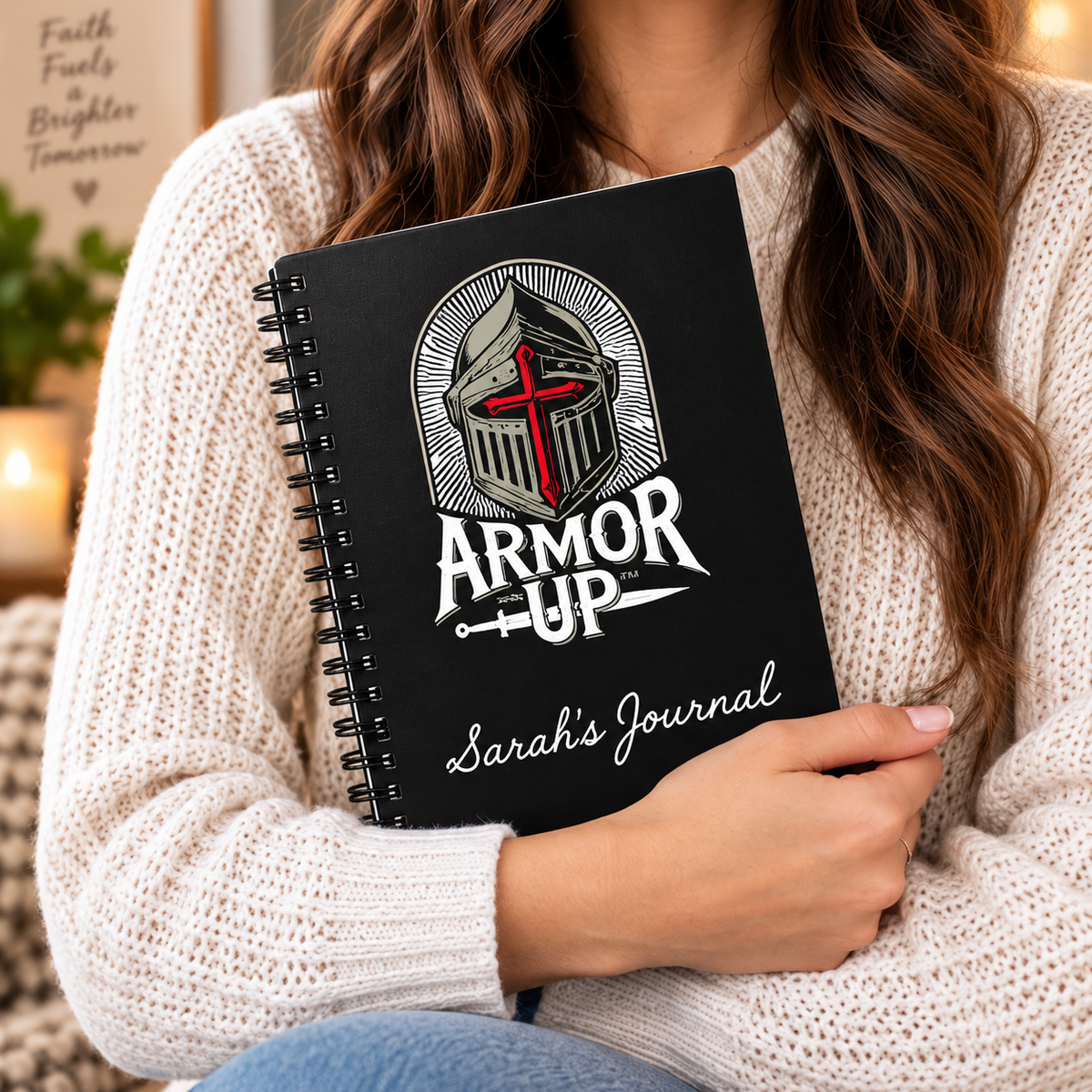 A woman in a cream knit sweater holds a black spiral-bound journal. The cover features a knight helmet graphic with a red cross and the text 'ARMOR UP' and 'Sarah's Journal'.
