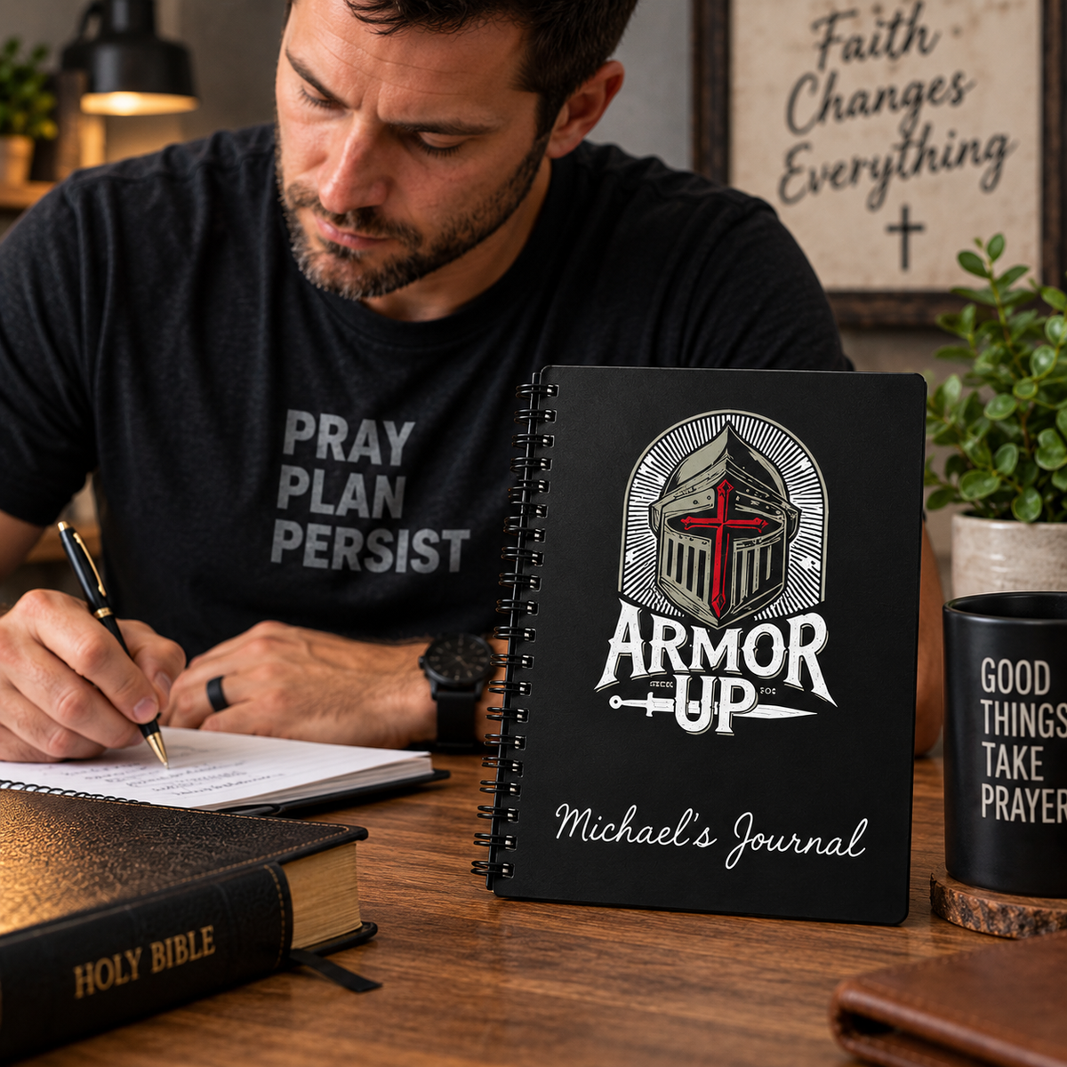 A man sitting at a wooden desk writing in a notebook, with a black spiral-bound journal titled 'Armor Up Michael's Journal' prominently displayed in the foreground. The journal features a graphic of a knight in armor with a red cross on a silver helmet.