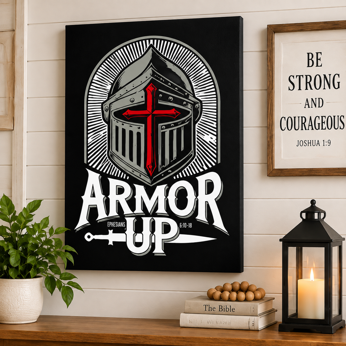A black canvas wall art print featuring a stylized medieval knight helmet with a red cross and the words 'ARMOR UP' is displayed on a white shiplap wall above a wooden shelf with a plant, books, and a lantern.