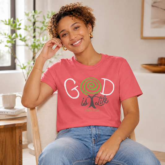 A woman sitting in a chair wearing a coral pink graphic t-shirt with 'GOD is Life' printed on the front, paired with blue jeans in a bright, modern living room setting.