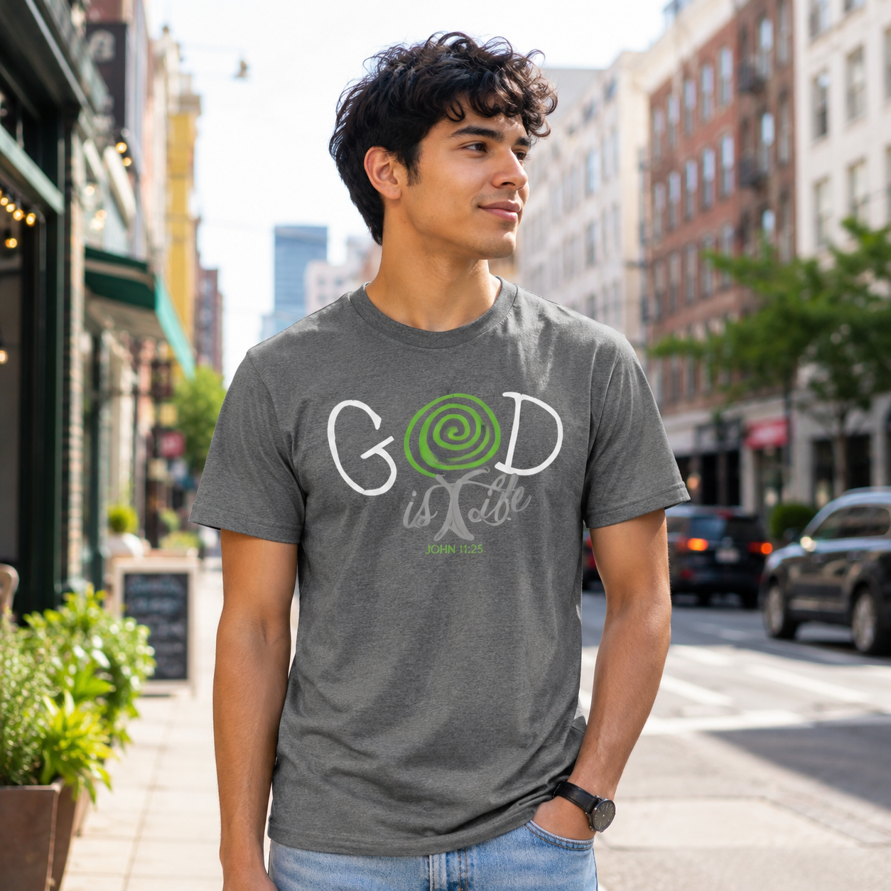 A man wearing a dark heather gray graphic t-shirt with a green and white 'God is life' tree design, standing on a city street.