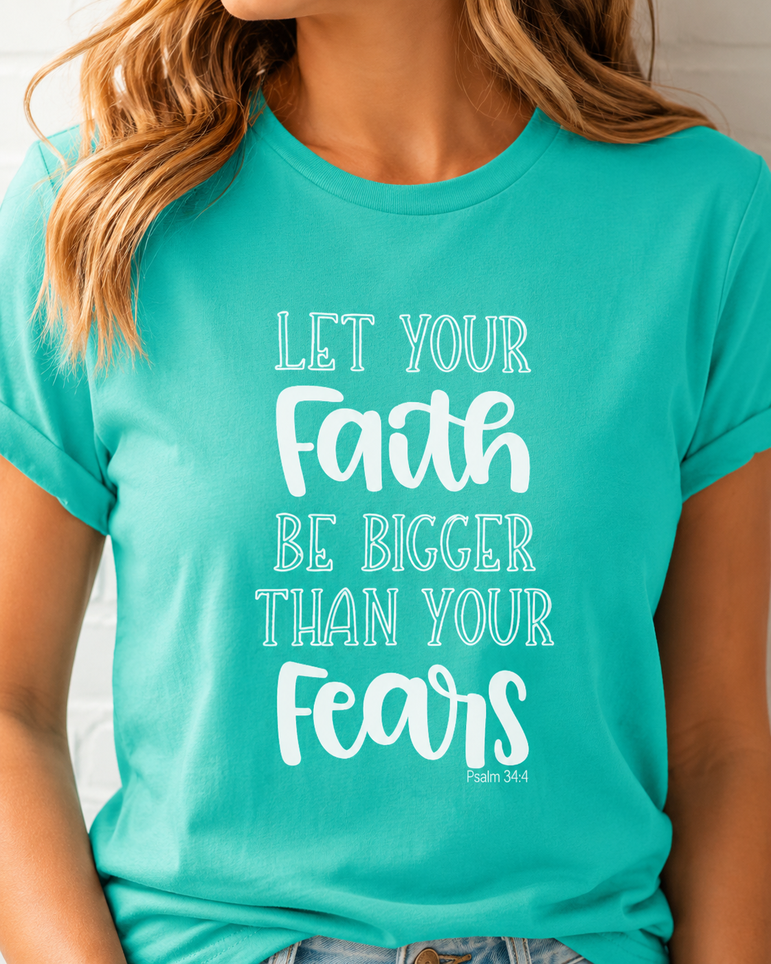 A woman wearing a bright turquoise t-shirt with the white printed text 'LET YOUR Faith BE BIGGER THAN YOUR Fears Psalm 34:4'.