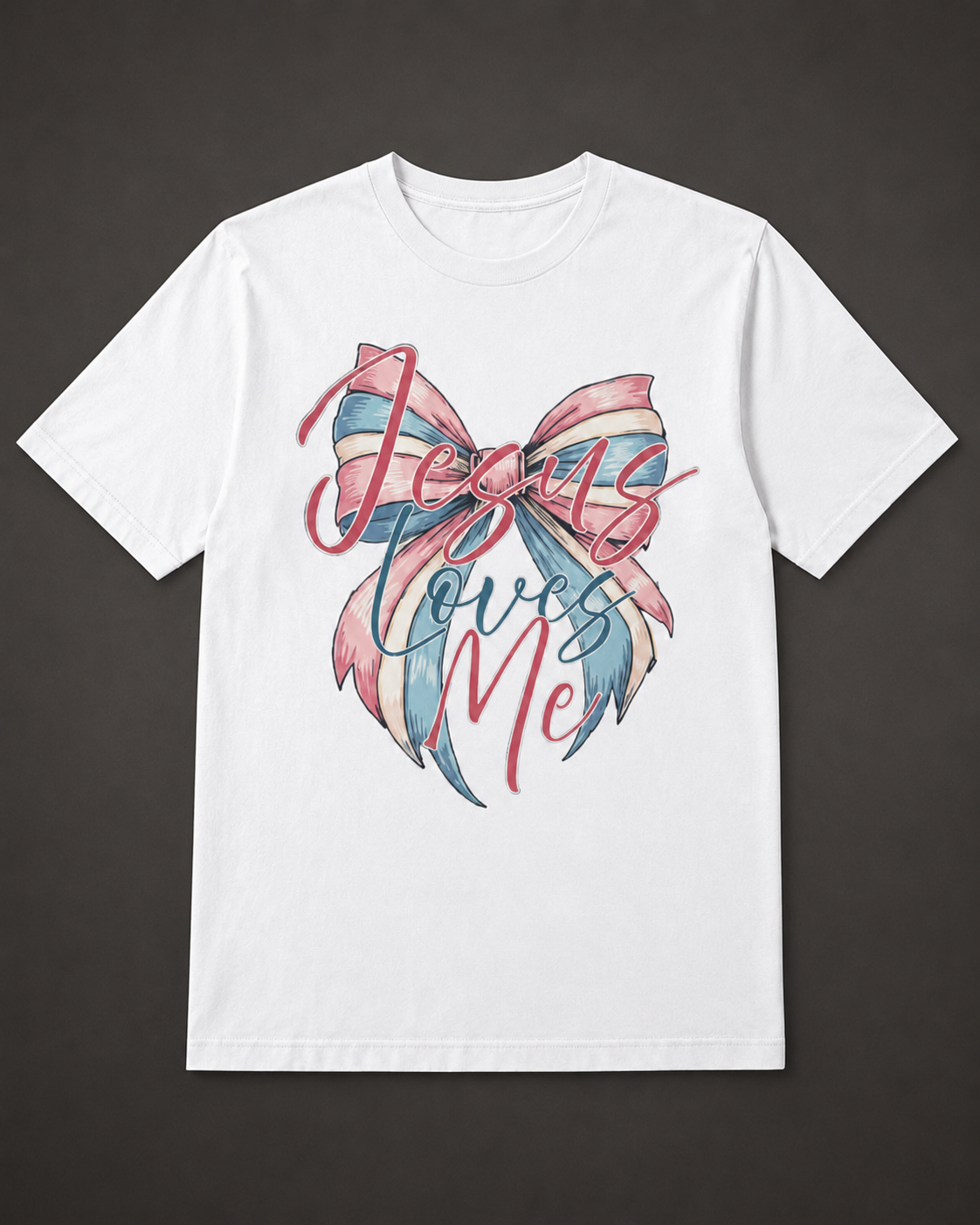 A white short-sleeve crewneck t-shirt with a graphic on the front featuring a pink and blue striped bow and the cursive text 'Jesus Loves Me' in pink and blue, displayed against a dark gray background.