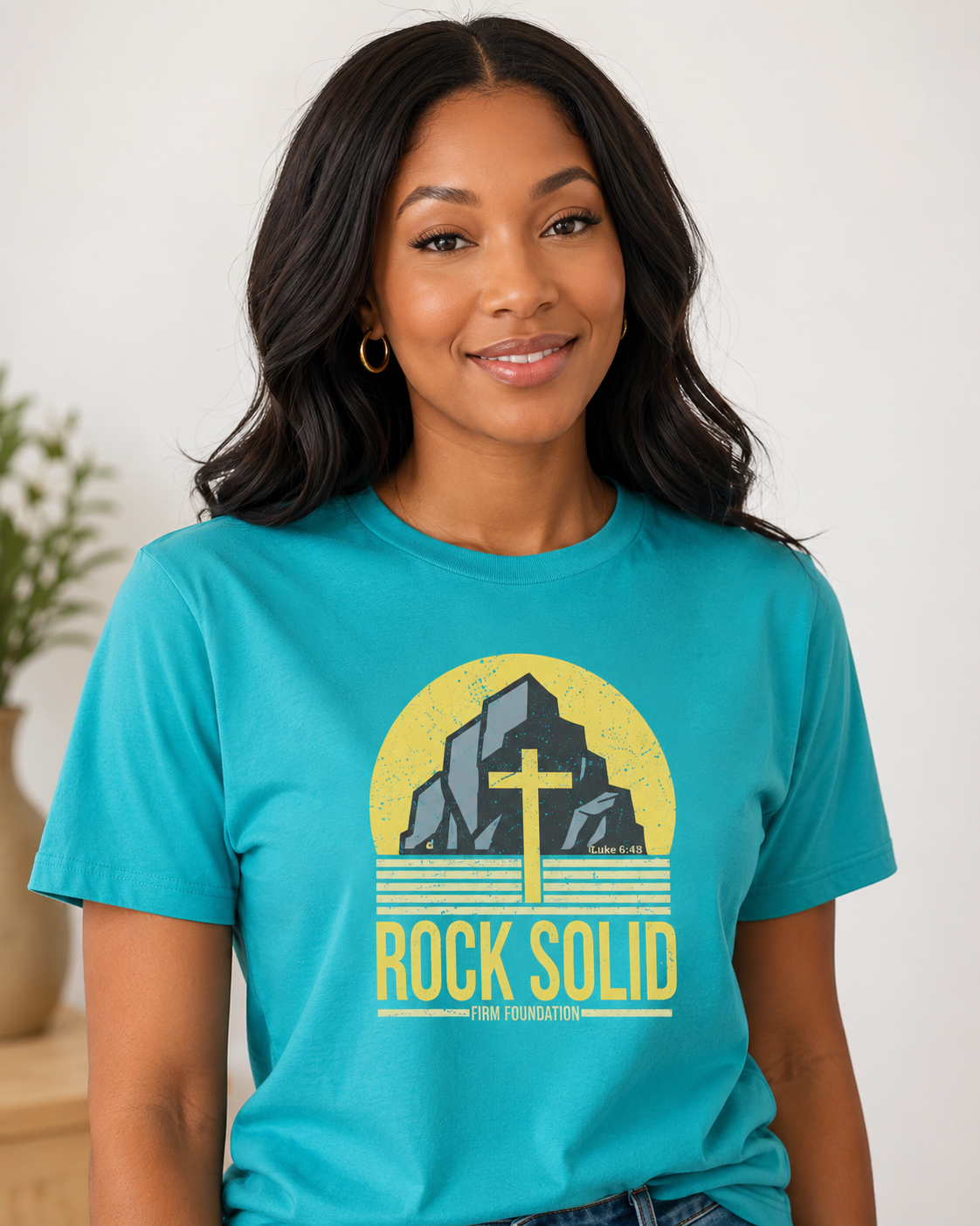 Black woman wearing a teal Rock Solid Christian T-shirt featuring a Luke 6:48 firm foundation design