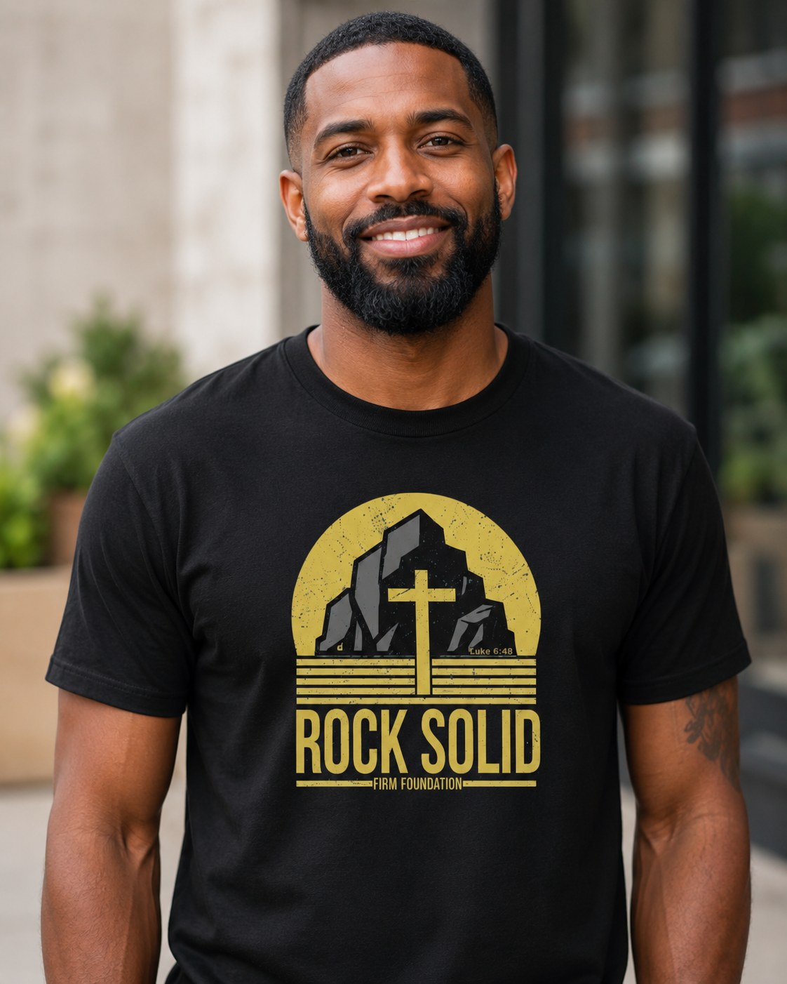 Black man wearing a black Rock Solid Christian T-shirt with a bold cross and Luke 6:48 design