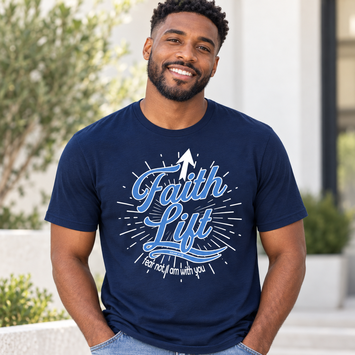 A smiling man wearing a navy blue graphic t-shirt with a light blue and white 'Faith Lift' design, standing outdoors in front of a modern building.