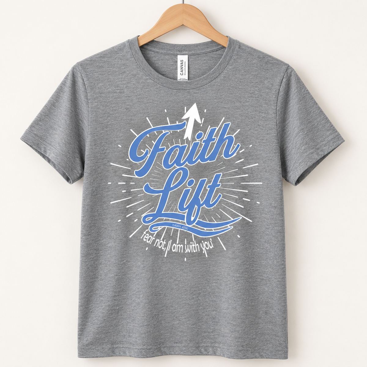 A heather gray short-sleeve t-shirt hanging on a wooden hanger against a light beige background. The shirt features a graphic on the front with the words 'Faith Lift' in blue script, a white upward-pointing arrow, and white rays, with the phrase 'Fear not, I am with you' in white script below.
