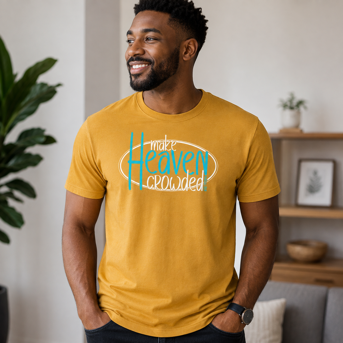 A man wearing a mustard yellow graphic t-shirt with the text 'make Heaven crowded' in white and light blue, standing in a modern living room setting.