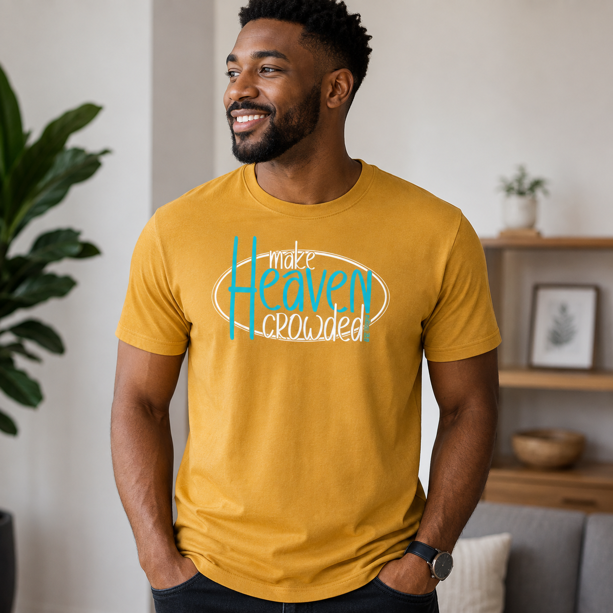 A man wearing a mustard yellow graphic t-shirt with the text 'make Heaven crowded' in white and light blue, standing in a modern living room setting.