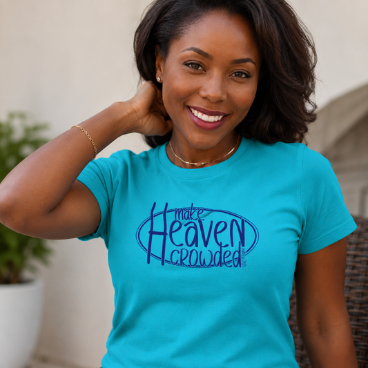A smiling woman wearing a bright turquoise short-sleeve t-shirt with a dark blue graphic that reads 'make Heaven crowded' on the chest, posed in an outdoor setting.
