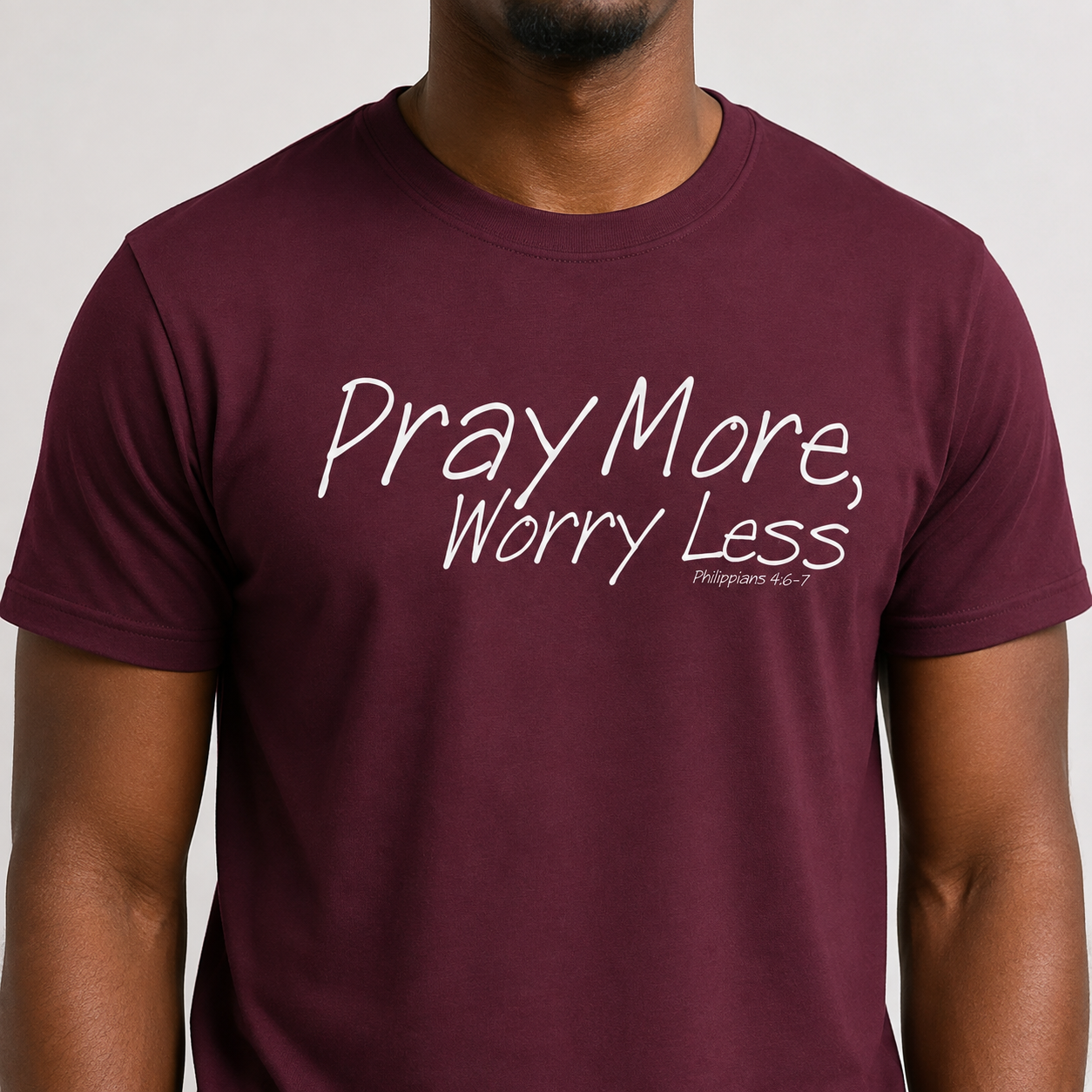A man wearing a maroon crewneck t-shirt with the white printed text 'Pray More, Worry Less' and 'Philippians 4:6' on the chest, shown against a light gray background.